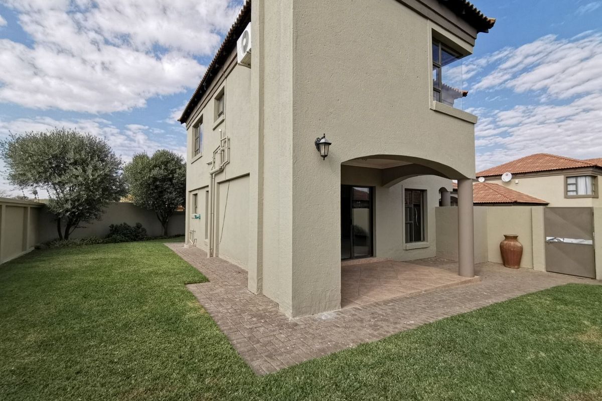 Rear view of the townhouse featuring a covered patio, paved walkway, and a well-maintained private garden area.