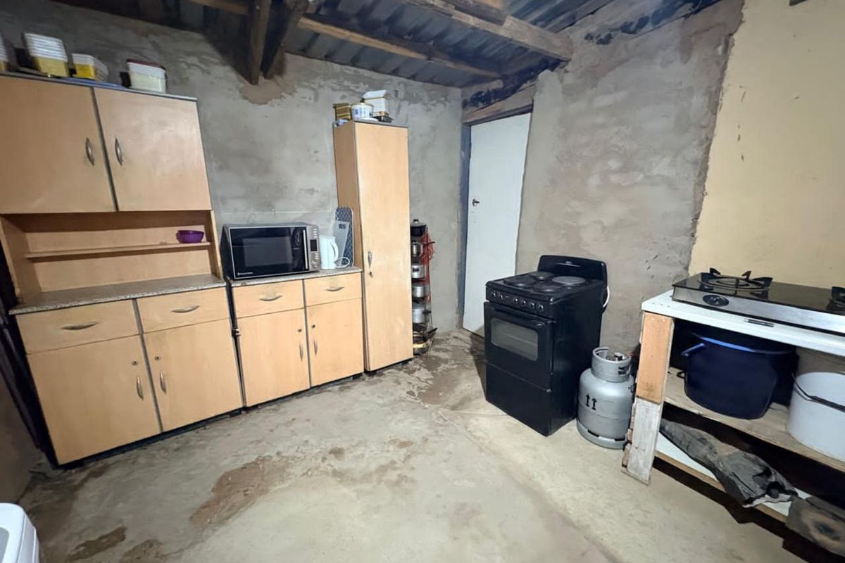 A rustic kitchen area featuring basic cabinetry, a freestanding stove, and exposed structural elements with unfinished concrete walls and flooring.