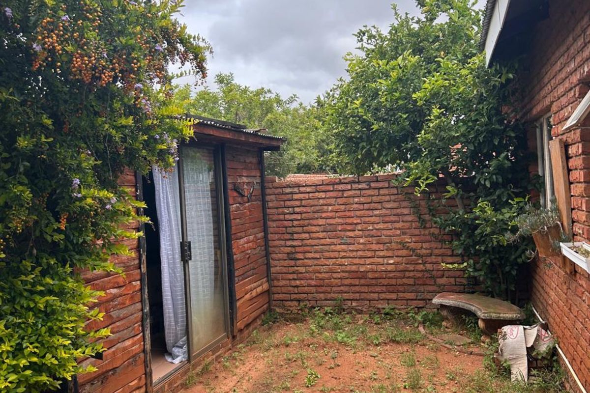 A private rear courtyard featuring a brick boundary wall, a small wooden outbuilding with sliding doors, and established garden greenery.
