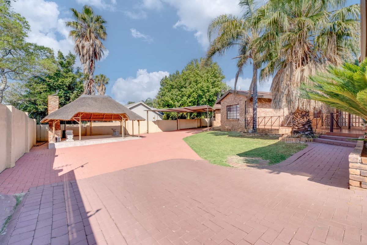 Spacious rear garden featuring a thatched lapa, paved entertainment area, covered carport, and established palm trees.