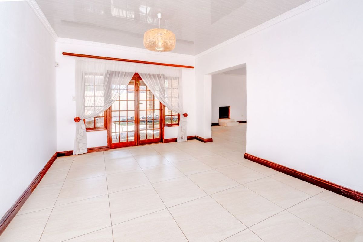 A bright, empty living room featuring large tiled flooring, a glossy ceiling finish, and timber-framed French doors leading to an outdoor area.