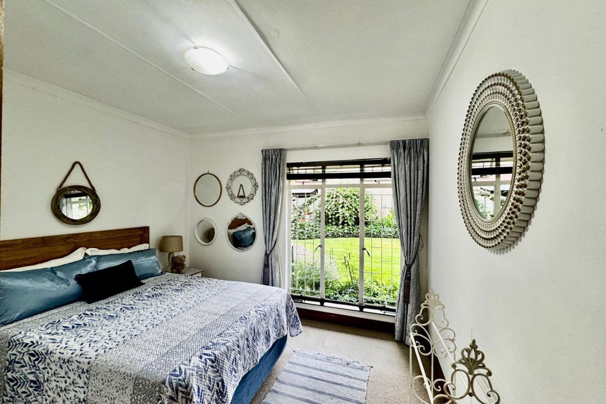 A bedroom featuring a large window with garden views, carpeted flooring, and a ceiling-mounted light fixture.