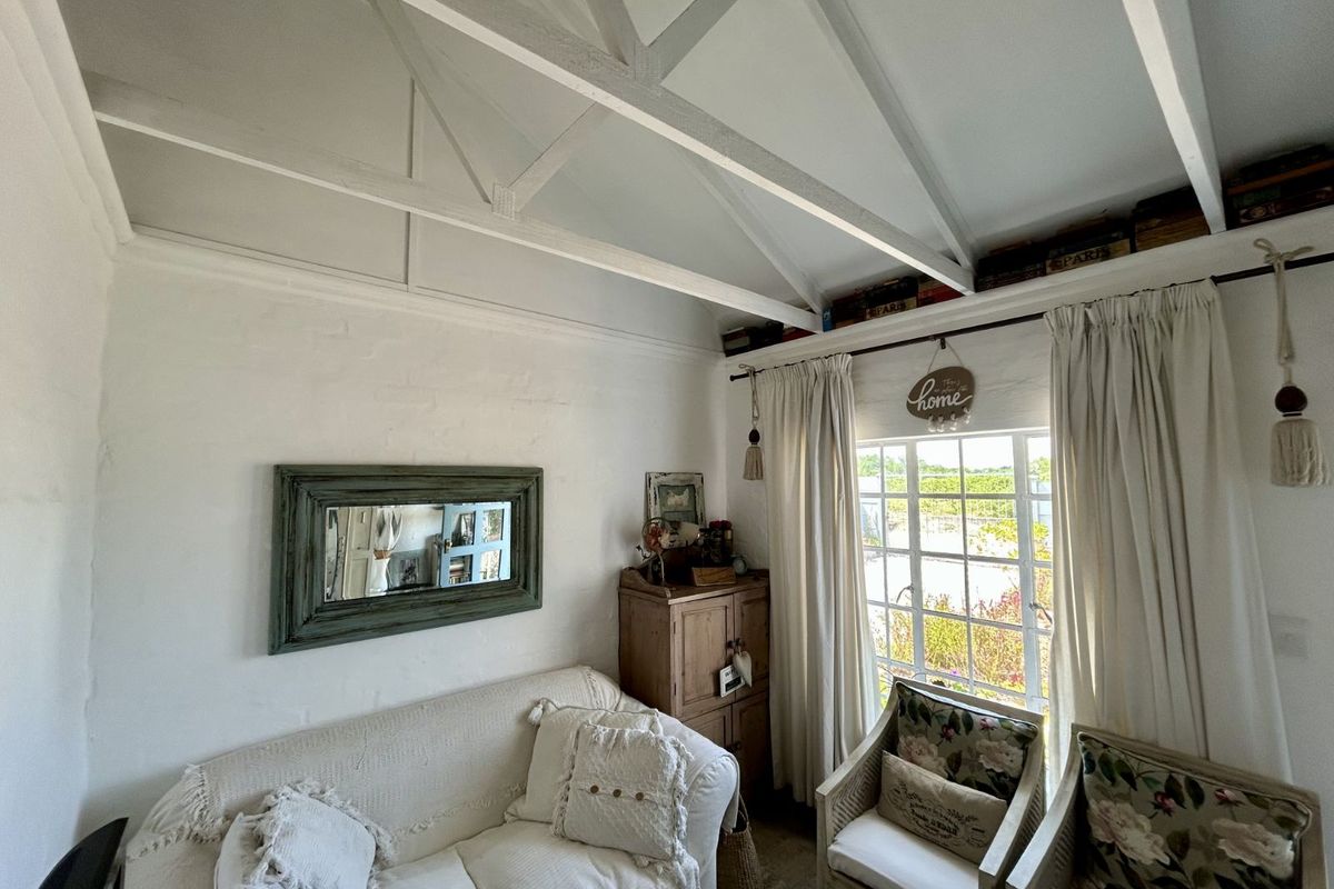 A cozy living room featuring a vaulted ceiling with exposed white beams, a large window with natural light, and painted brick walls.