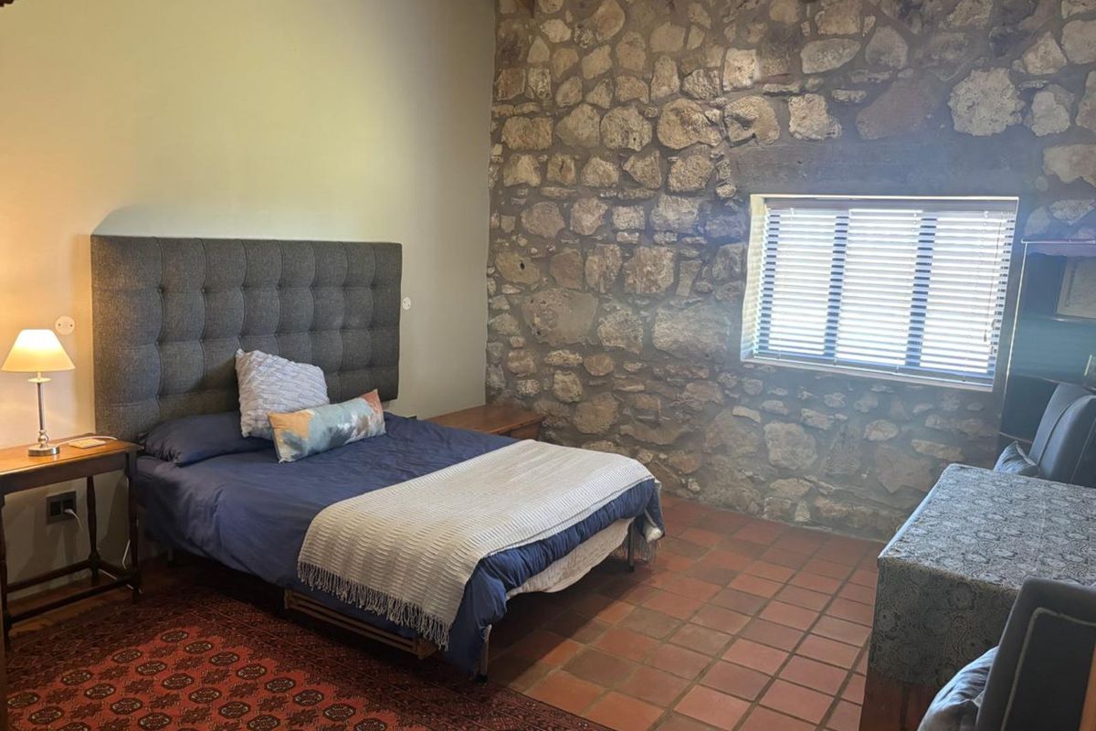A rustic bedroom featuring exposed natural stone walling, terracotta tile flooring, and exposed timber ceiling beams, creating a warm and characterful living space.