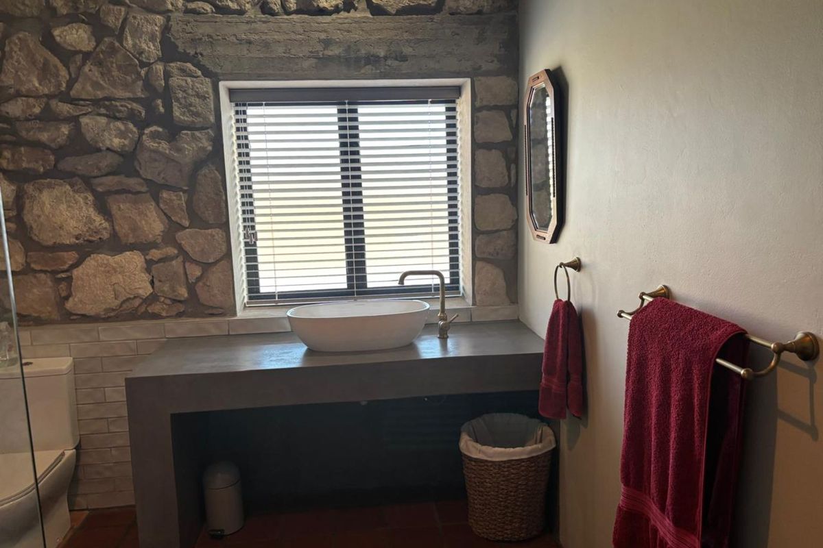 A rustic bathroom featuring a stone feature wall, a concrete vanity with a vessel sink, and terracotta floor tiles.