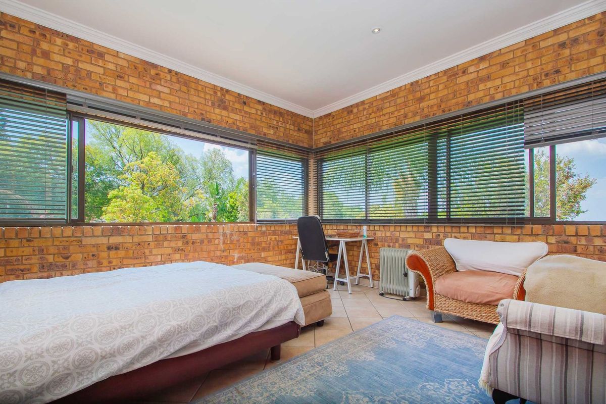 Spacious bedroom featuring exposed brick walls, large windows with venetian blinds, and tiled flooring, offering plenty of natural light and garden views.