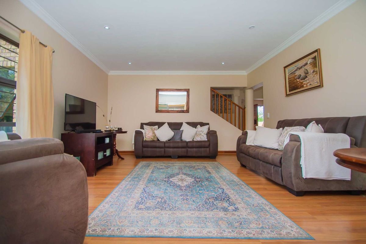 A spacious living room featuring warm-toned laminate flooring, recessed ceiling lighting, and a staircase with a wooden balustrade leading to the upper level.