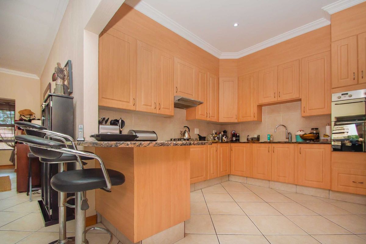 A functional kitchen featuring light wood cabinetry, granite countertops, a built-in oven, extractor fan, and tiled flooring with a breakfast bar area.