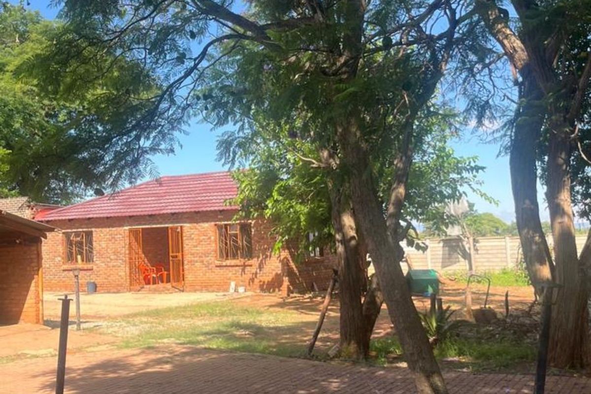 A view of the rear exterior of the farm property, featuring a brick building, paved courtyard area, and mature trees.