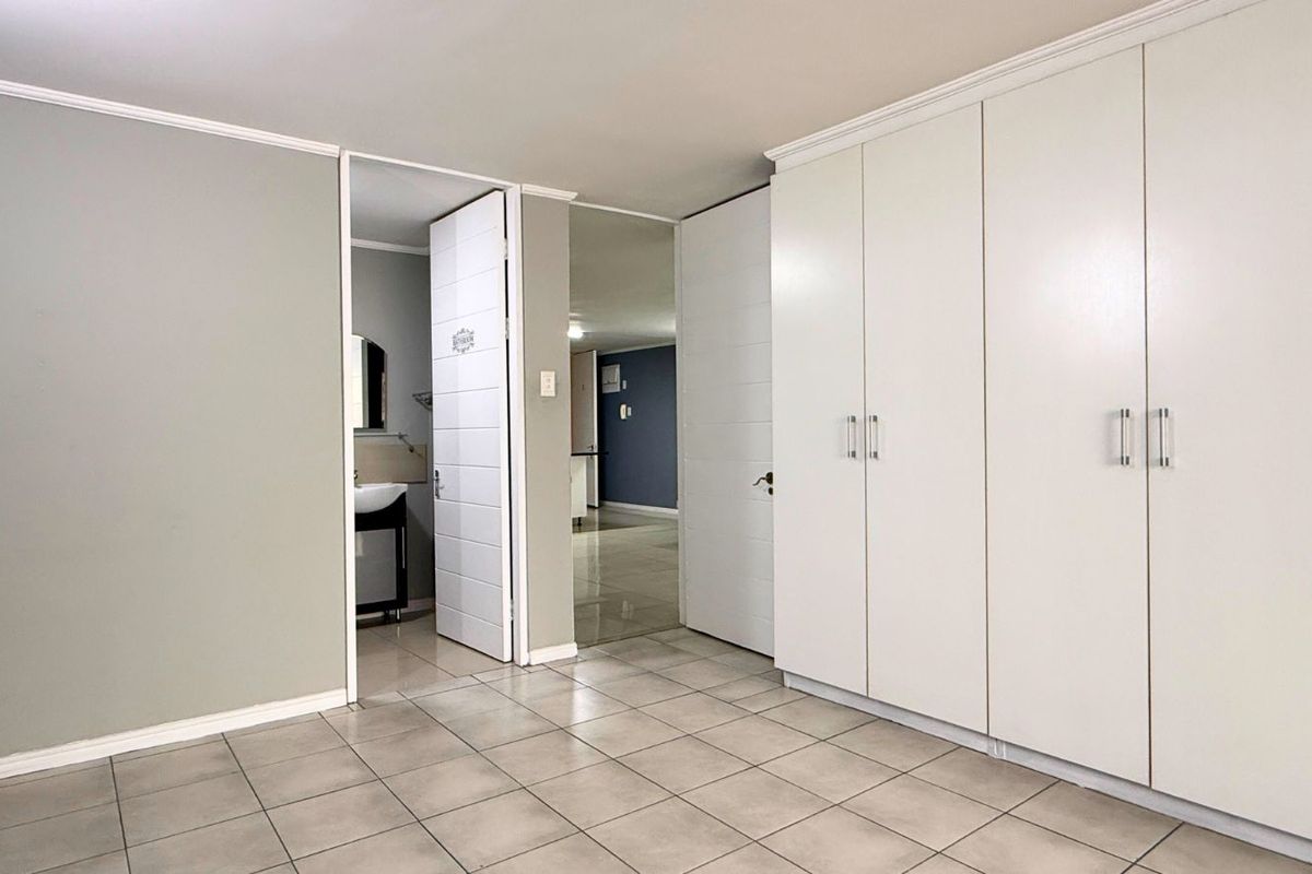 A clean bedroom interior featuring built-in floor-to-ceiling wardrobes, tiled flooring, and access to an adjoining bathroom.