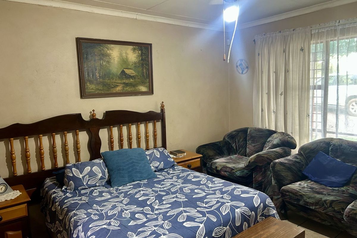 A bedroom featuring tiled flooring, a ceiling fan, and large windows with curtains, providing a functional and lived-in space.