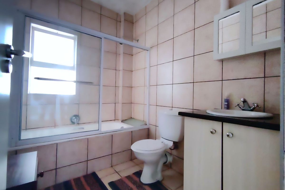 A functional bathroom featuring a bathtub with a glass shower screen, a toilet, and a vanity cabinet with an integrated basin.