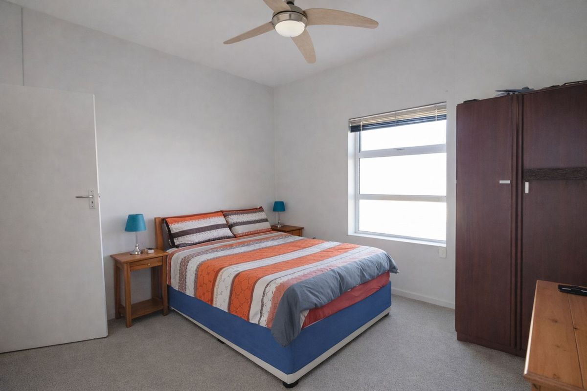 A functional bedroom featuring neutral carpeting, a ceiling fan, and a window providing natural light.