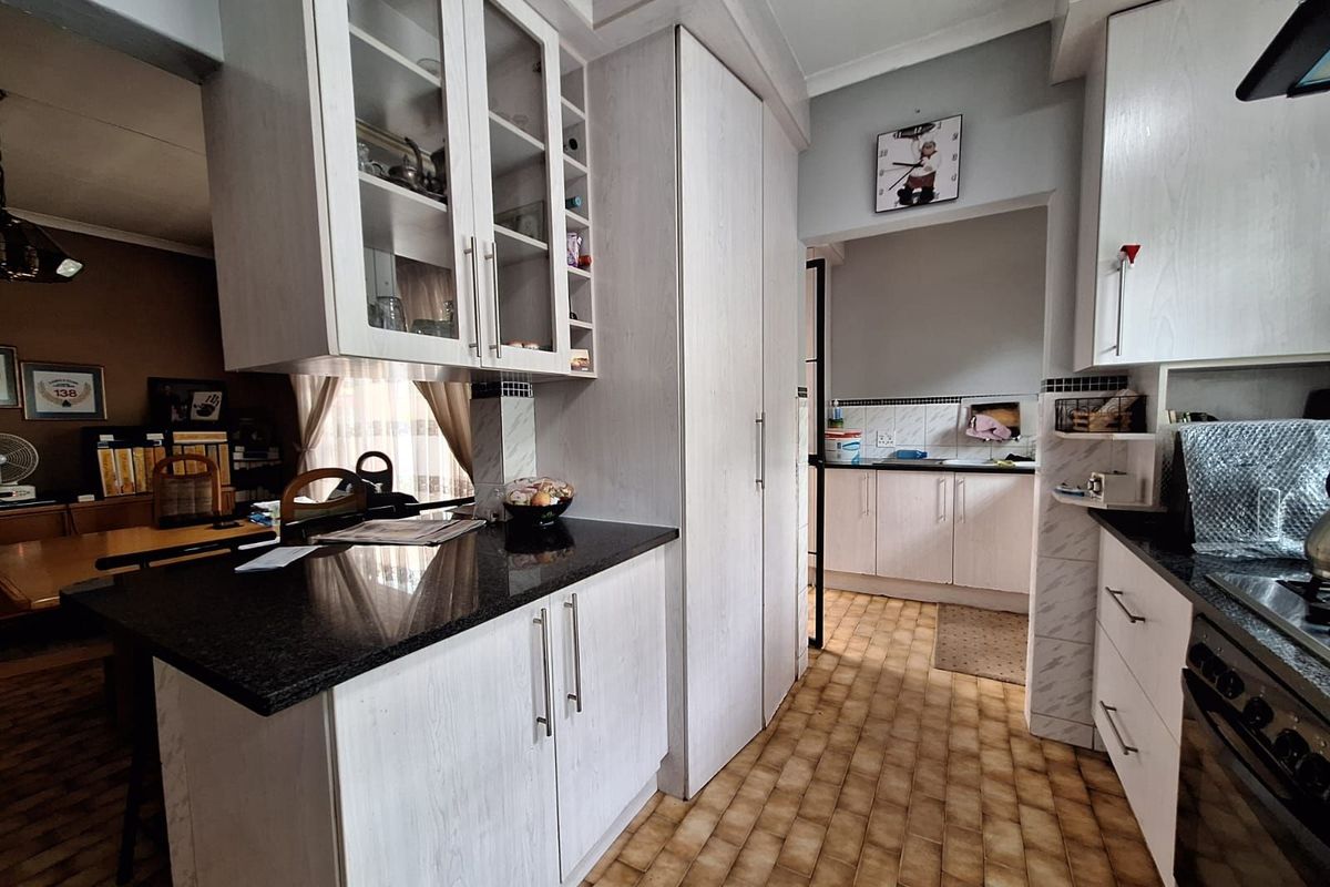 A functional kitchen featuring light-toned cabinetry, dark granite countertops, and a connected scullery area with additional storage and workspace.