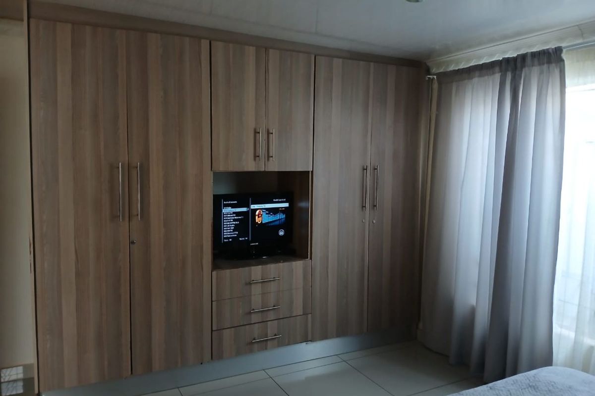 A bedroom featuring extensive built-in wooden cabinetry with integrated shelving and storage, complemented by tiled flooring and neutral window treatments.