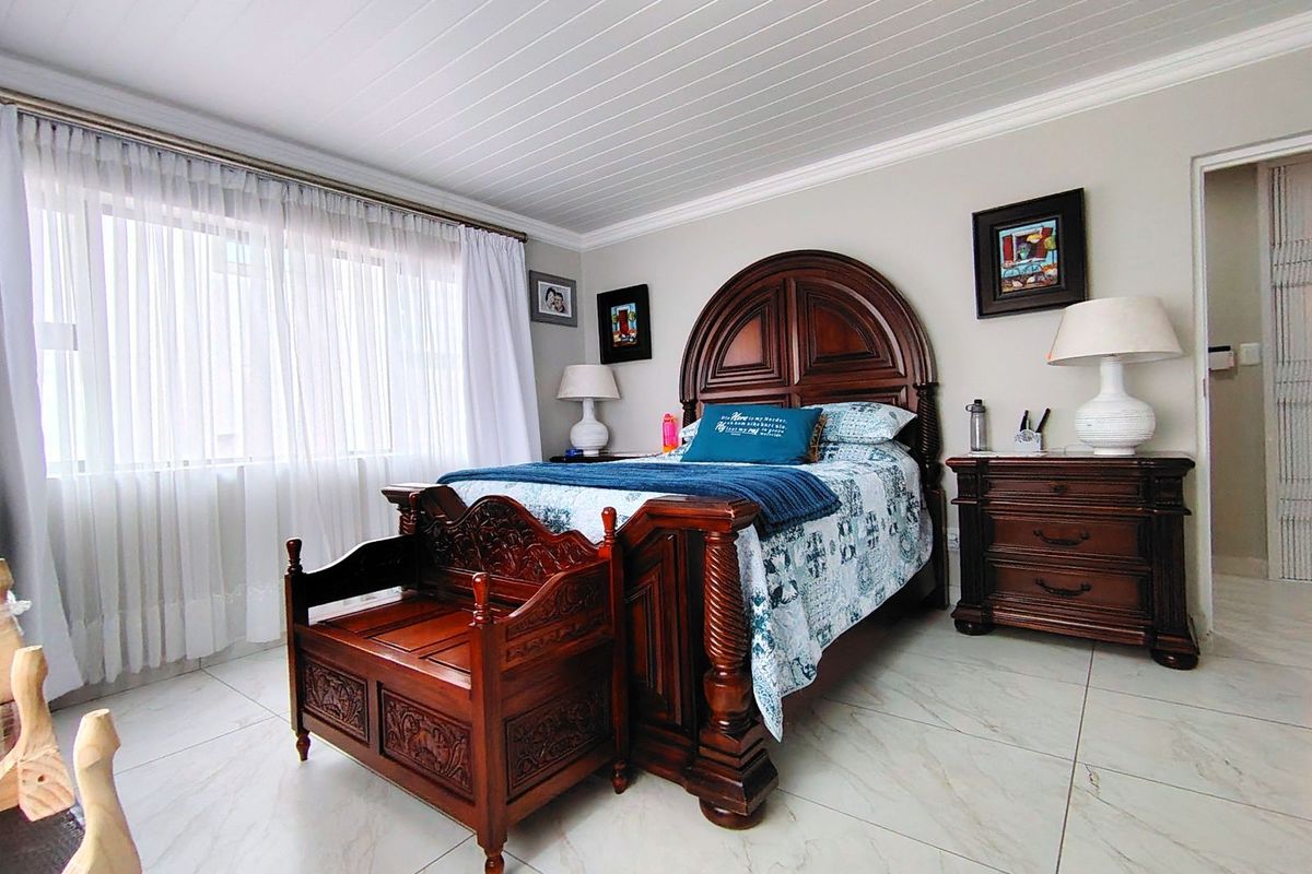 A well-maintained bedroom featuring light-colored floor tiles, a white tongue-and-groove ceiling, and large windows allowing for ample natural light.