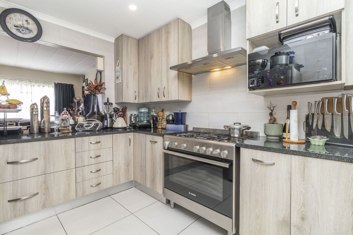 A functional kitchen featuring light wood-grain cabinetry, dark granite countertops, tiled splashbacks, and a stainless steel gas stove with an integrated extractor fan.