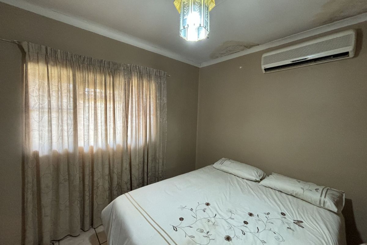 A bedroom featuring a wall-mounted air conditioning unit and tiled flooring, showing signs of ceiling water damage.