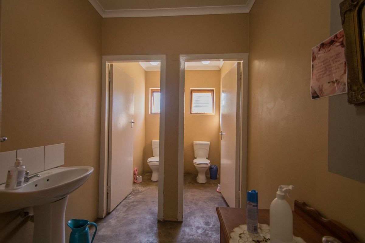 A functional bathroom area featuring a pedestal basin and two separate toilet cubicles with natural lighting.