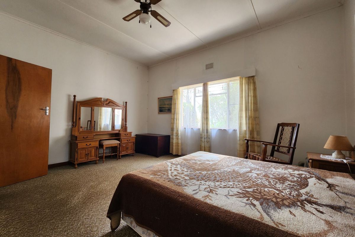 A spacious bedroom featuring a ceiling fan, large window with natural light, and carpeted flooring, offering a blank canvas for modernization.
