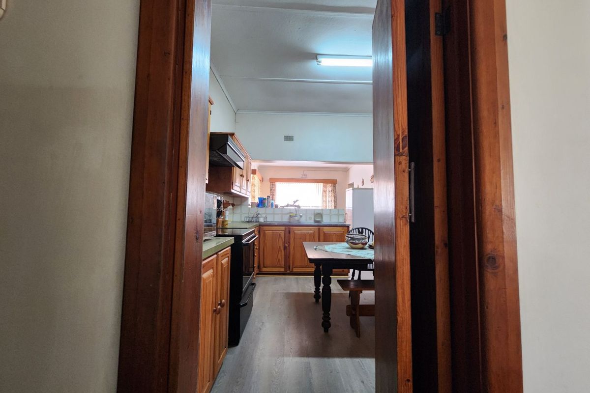 A view into a functional kitchen featuring wooden cabinetry, a built-in oven, and a dining area, viewed through a wooden door frame.