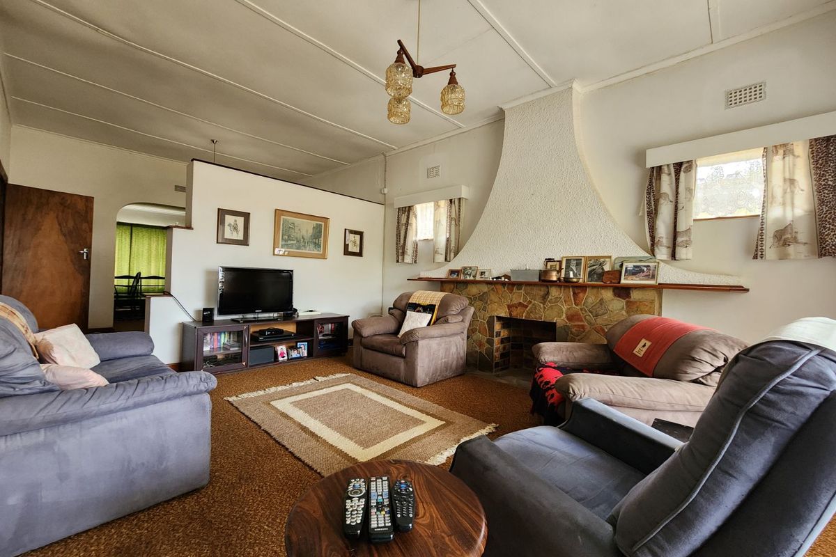 A spacious living room featuring a prominent stone fireplace, high ceilings, and a semi-open plan layout connecting to adjacent living areas.