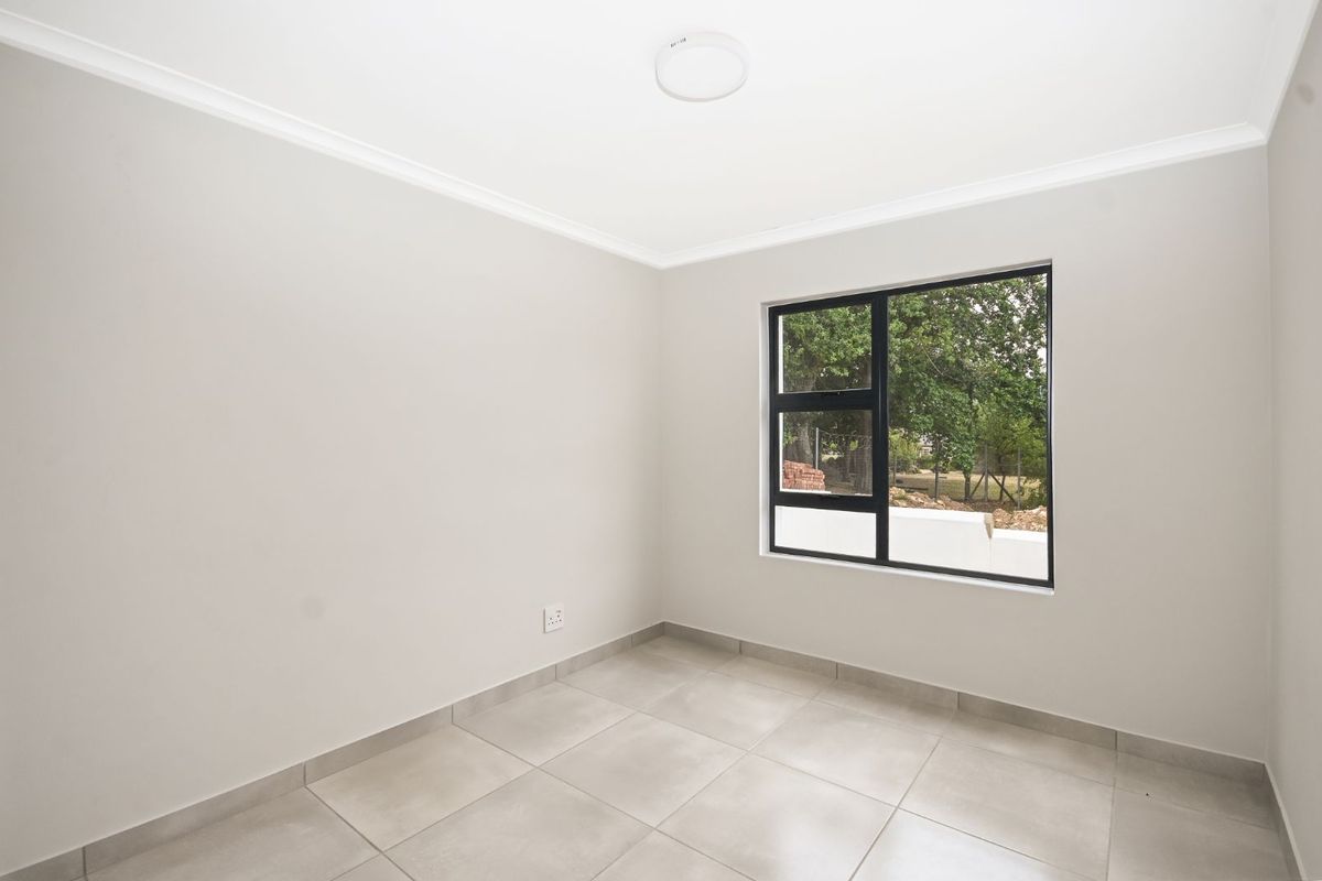 A bright, empty bedroom featuring neutral wall paint, large format floor tiles, and a modern black-framed window.