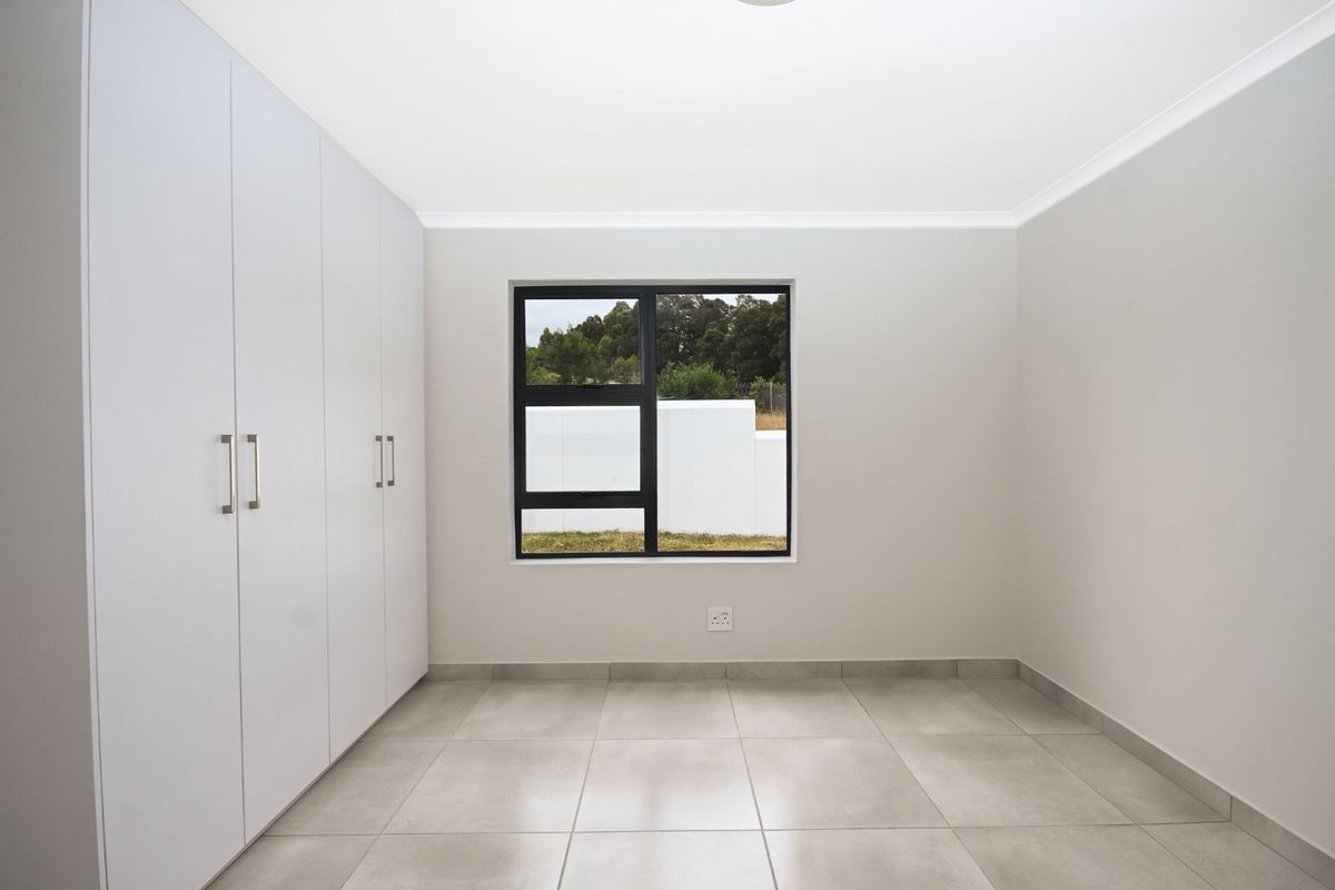 A bright, empty bedroom featuring neutral tiled flooring, built-in white cabinetry, and a modern black-framed window.