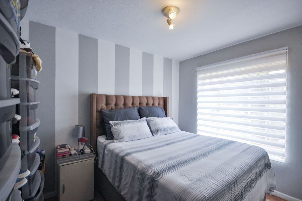 A bedroom featuring a striped accent wall, a window with fitted roller blinds, and a ceiling-mounted spotlight fixture.