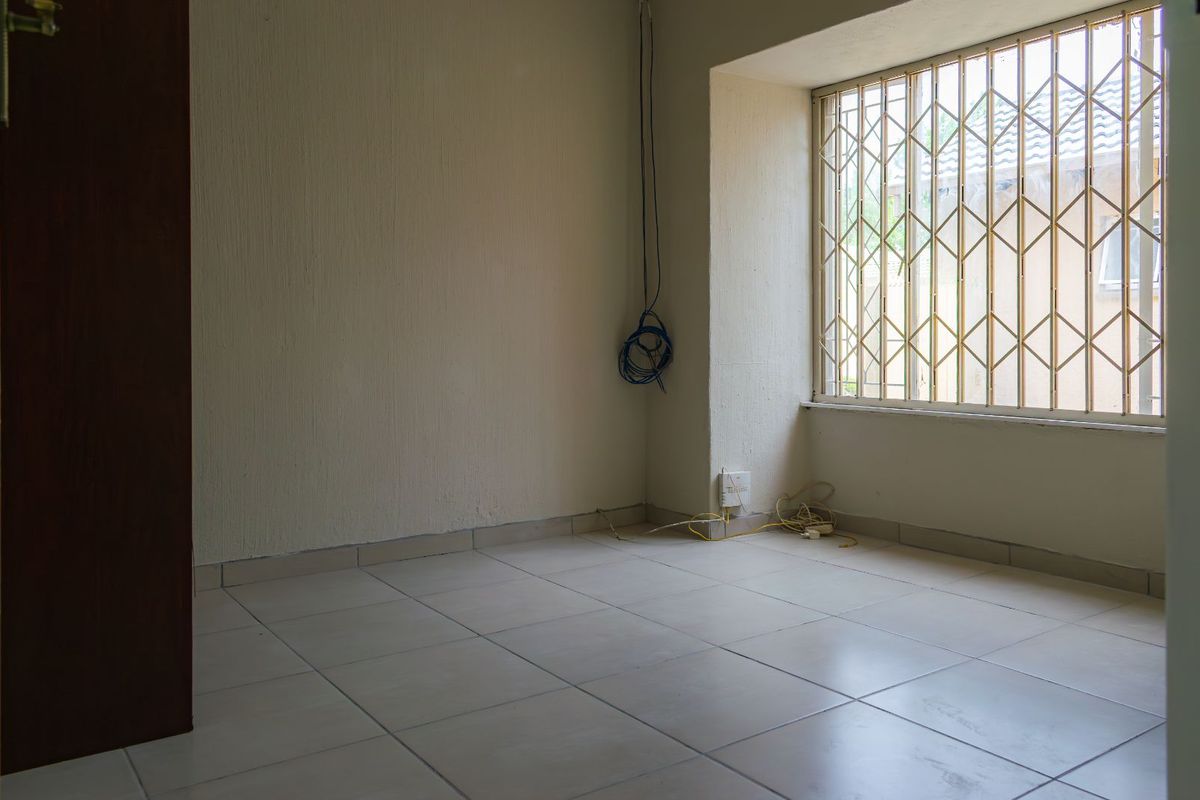 An empty room featuring tiled flooring and a window secured with a metal security gate.