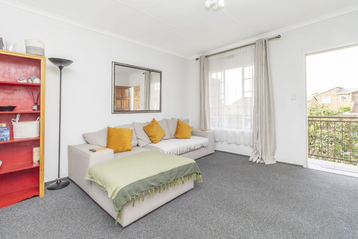 A bright living room featuring grey carpeting, large windows, and direct access to a private balcony.