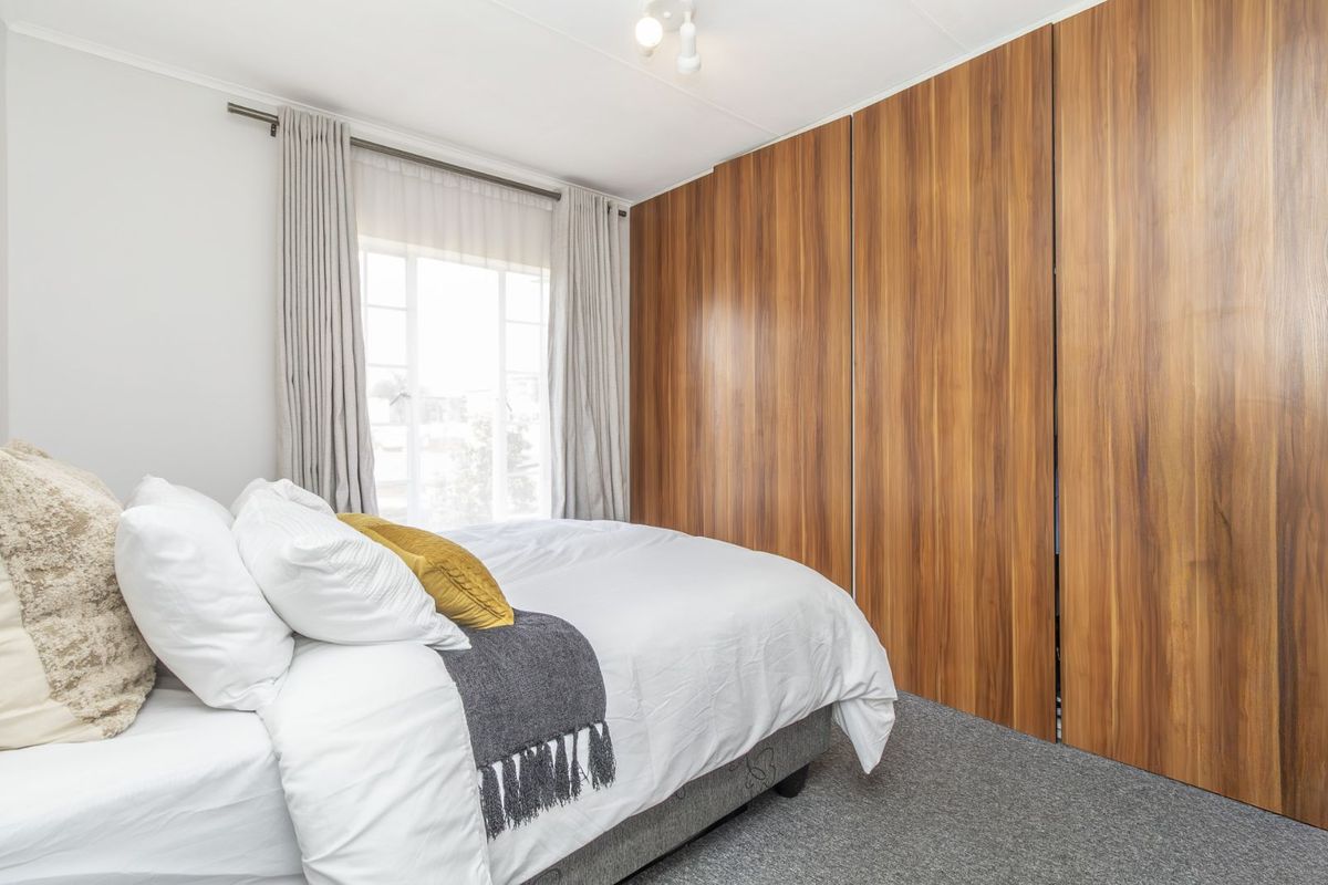 A well-maintained bedroom featuring floor-to-ceiling wood-finish built-in cupboards and neutral carpeting, offering a clean and functional living space.