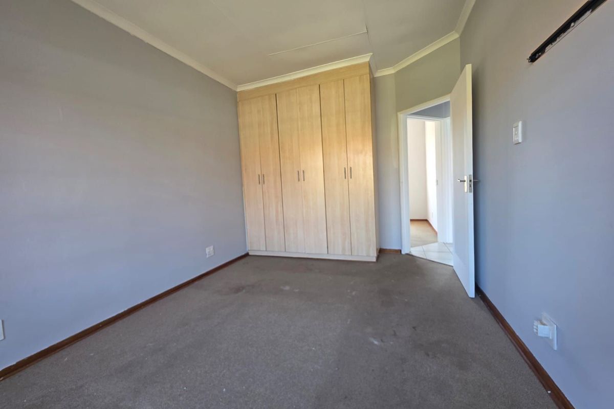 A vacant bedroom featuring built-in wooden cupboards, neutral wall paint, and carpeted flooring, with an open doorway leading to an adjacent hallway.