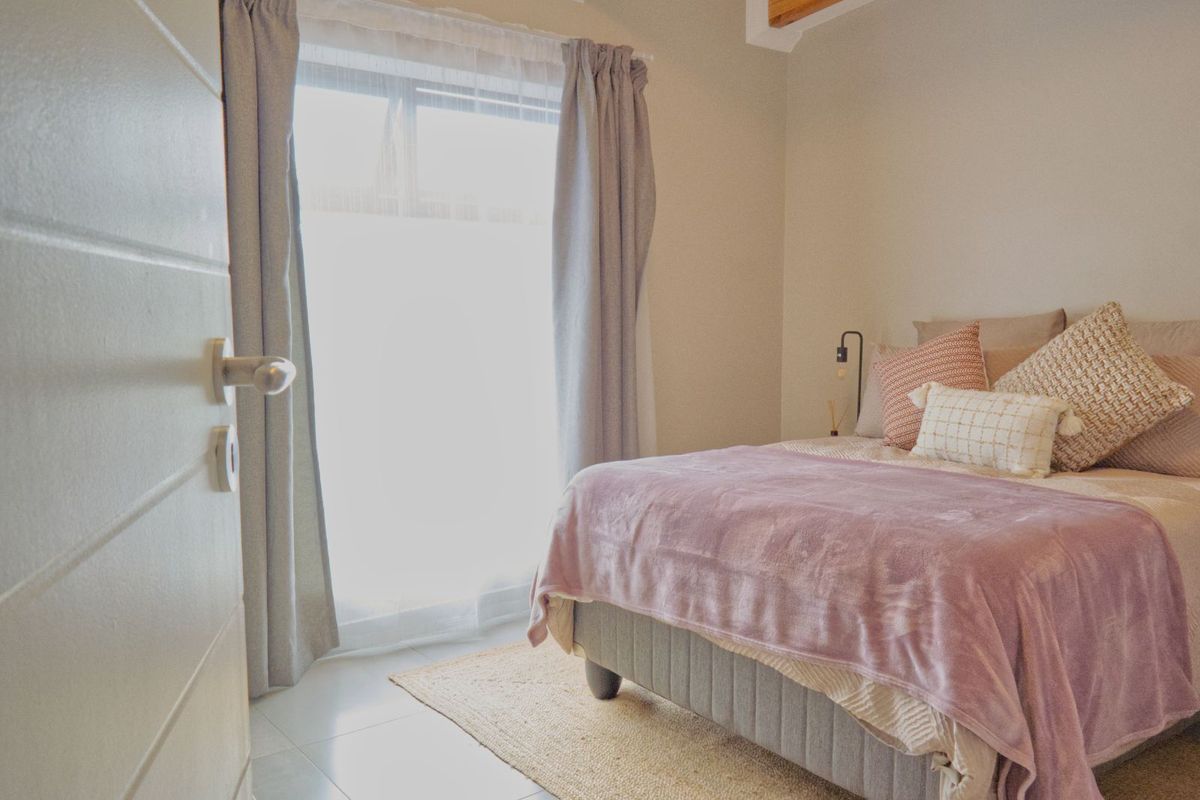 A bright and cozy bedroom featuring neutral tones, tiled flooring, and a large window allowing for ample natural light.