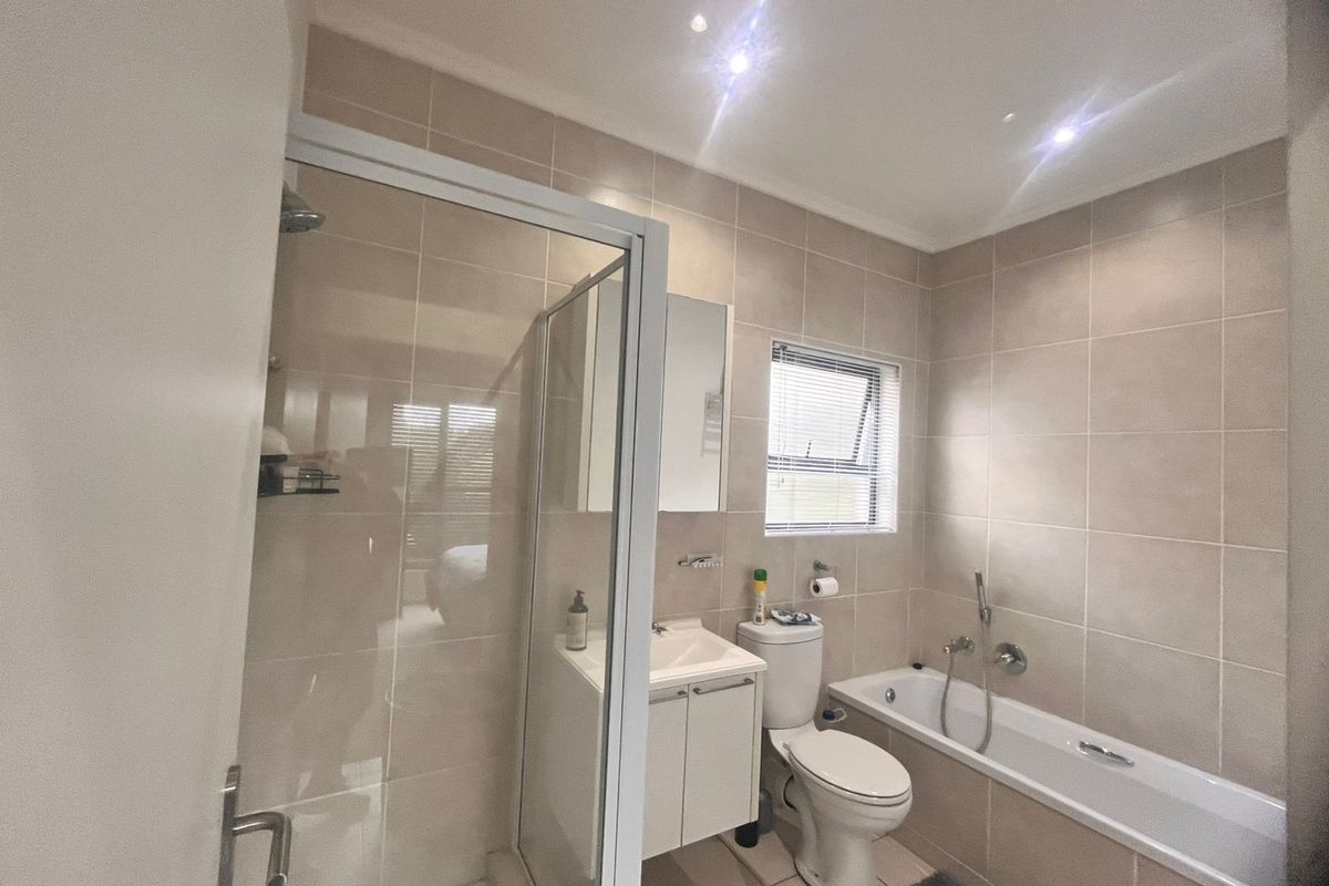 A modern bathroom featuring a glass-enclosed shower, a built-in bathtub with handheld showerhead, a vanity basin, and a toilet with neutral wall tiling.