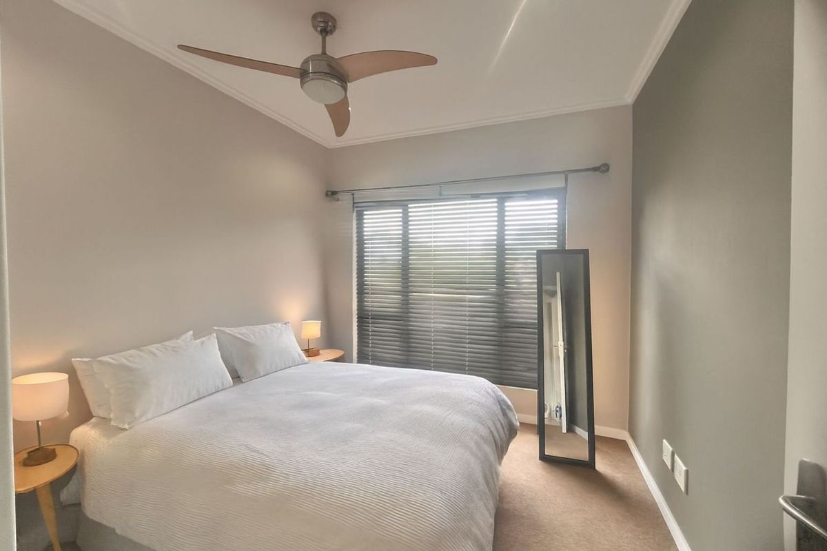 A well-maintained bedroom featuring neutral wall tones, carpeted flooring, a ceiling fan, and large windows with fitted blinds.