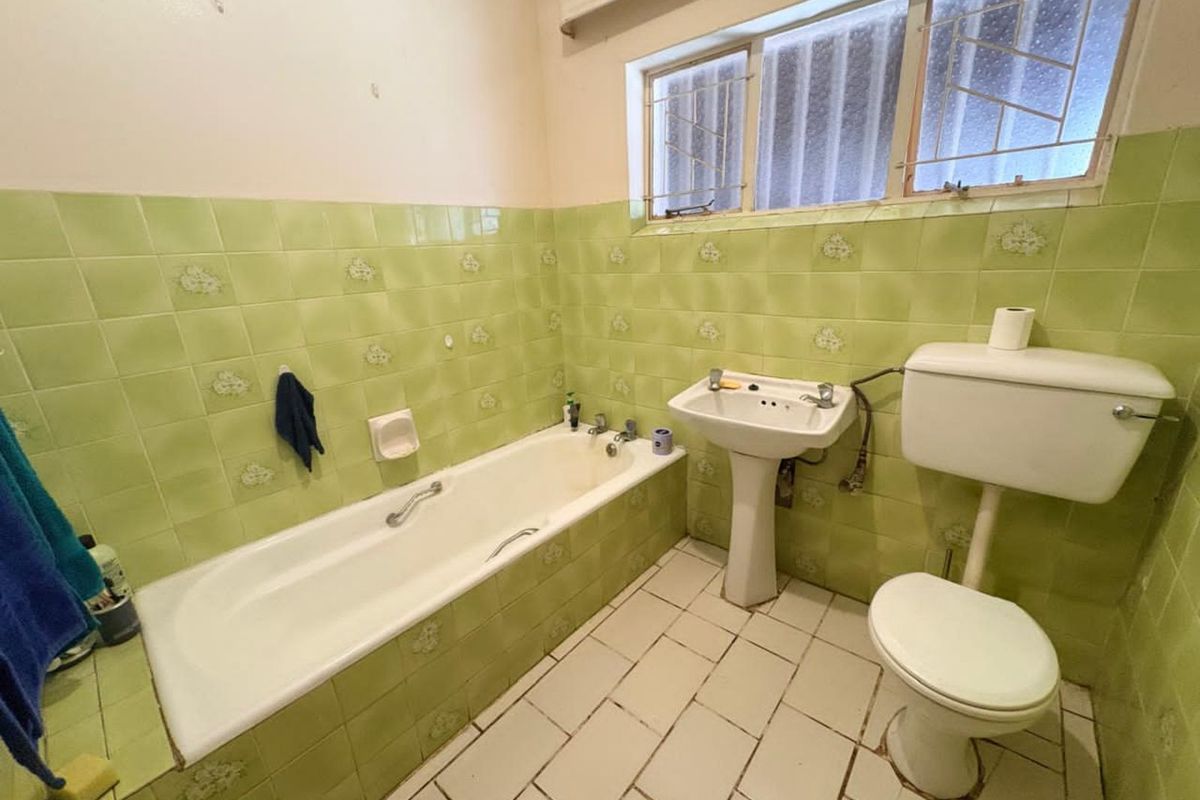 A dated bathroom featuring a green tiled bathtub, pedestal basin, and standard toilet, requiring modernization of finishes and fixtures.