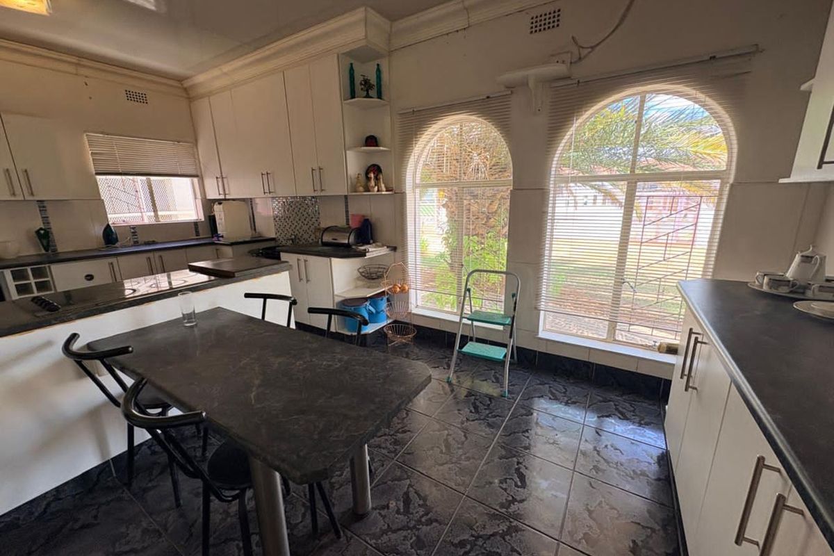 A functional kitchen featuring white cabinetry, dark countertops, and distinctive arched windows that provide natural light and garden views.