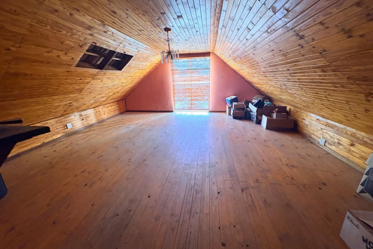 Spacious attic room featuring vaulted timber-clad ceilings, polished wooden flooring, and a skylight, offering a versatile living or storage space.