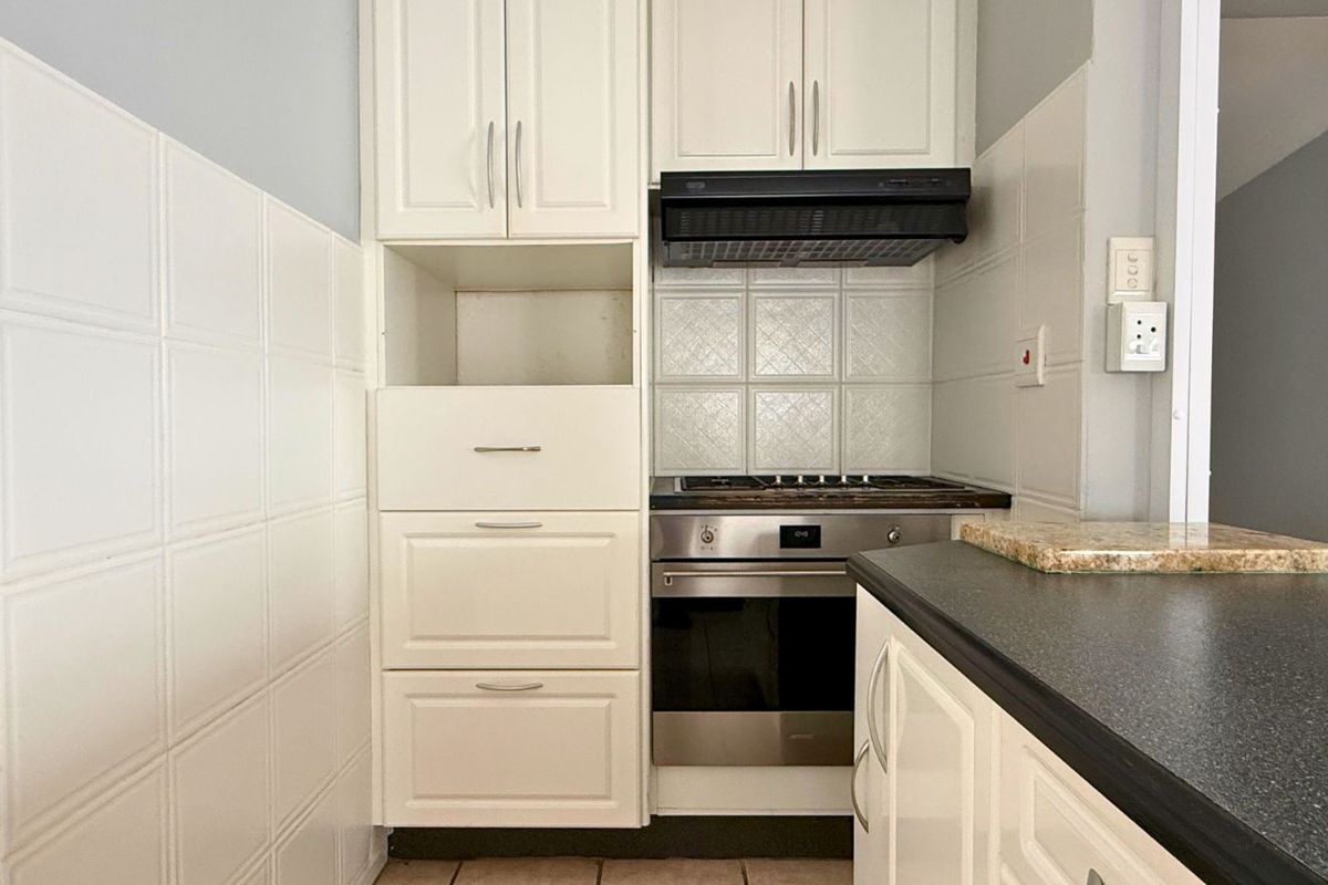 Compact kitchen featuring white cabinetry, built-in oven, gas hob, extractor fan, and dark laminate countertops with tiled splashbacks.