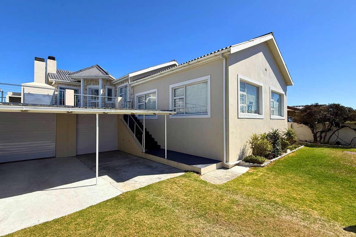 Exterior view of the property featuring a double garage, paved driveway, external staircase, and a well-maintained lawn area.