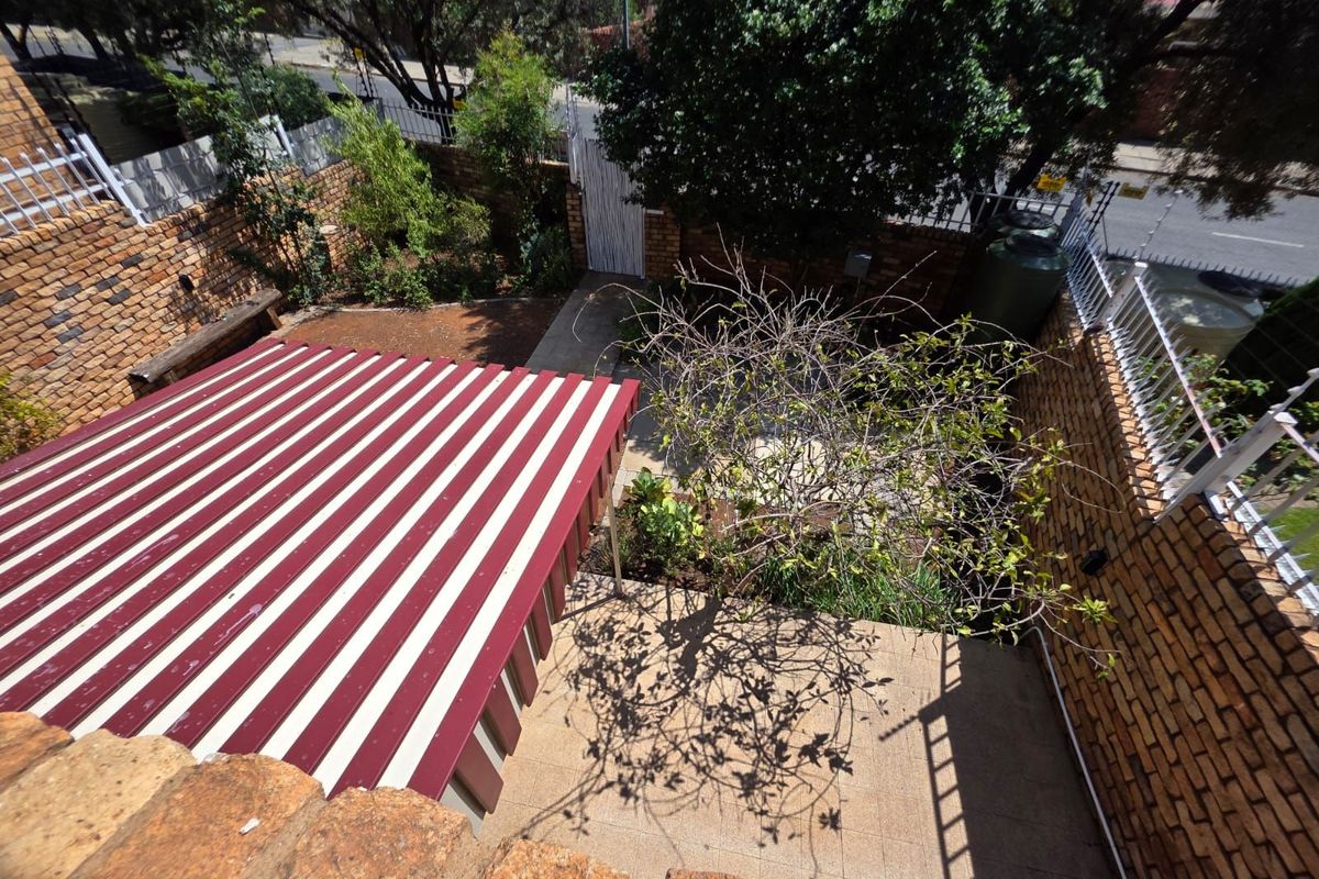 An elevated view of a private courtyard featuring a paved patio area, a striped retractable awning, and perimeter brick boundary walls.