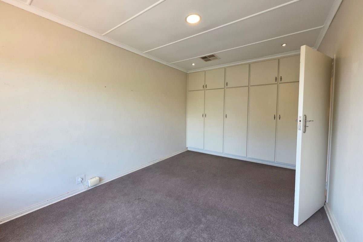 A spacious bedroom featuring neutral walls, fitted floor-to-ceiling built-in cupboards, recessed ceiling lighting, and carpeted flooring.