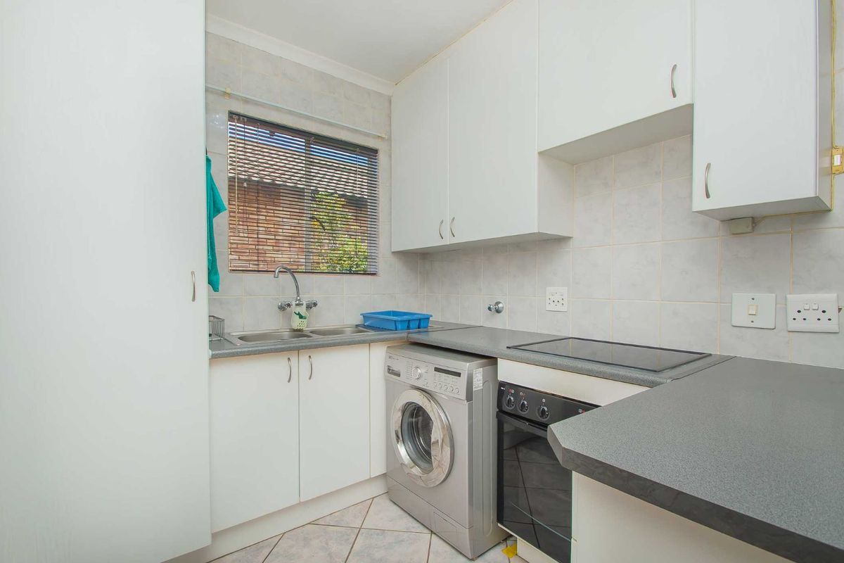 Compact kitchen featuring white cabinetry, grey laminate countertops, a built-in oven with hob, and integrated laundry plumbing.