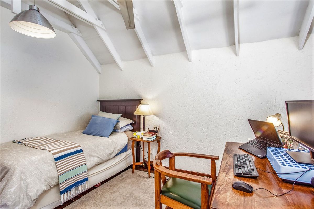 A cozy bedroom featuring a vaulted ceiling with exposed white rafters and textured walls, providing a bright and functional living space.