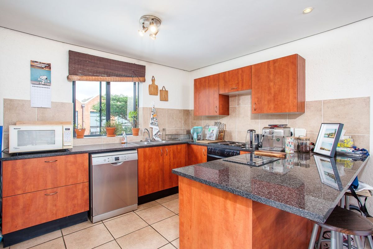 A functional kitchen featuring wood-finish cabinetry, granite countertops, tiled flooring, and a built-in hob with an extractor fan.