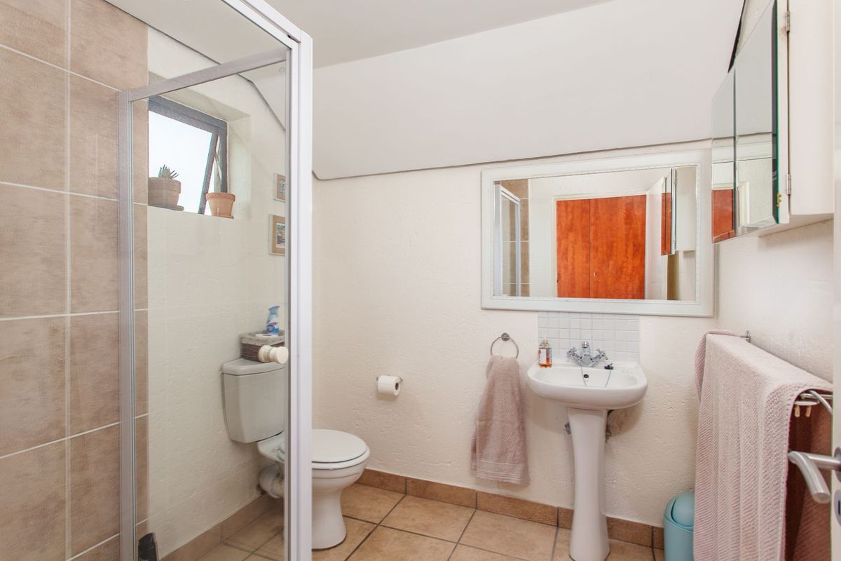A functional bathroom featuring a pedestal sink, a toilet, and a shower enclosure with tiled walls and flooring.