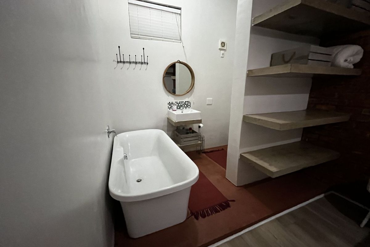 A bathroom featuring a freestanding bathtub, wall-mounted basin, and built-in concrete shelving units with a rustic aesthetic.