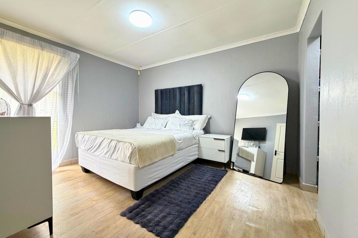 A well-maintained bedroom featuring light wood-look flooring, neutral grey walls, and a sliding door providing natural light.