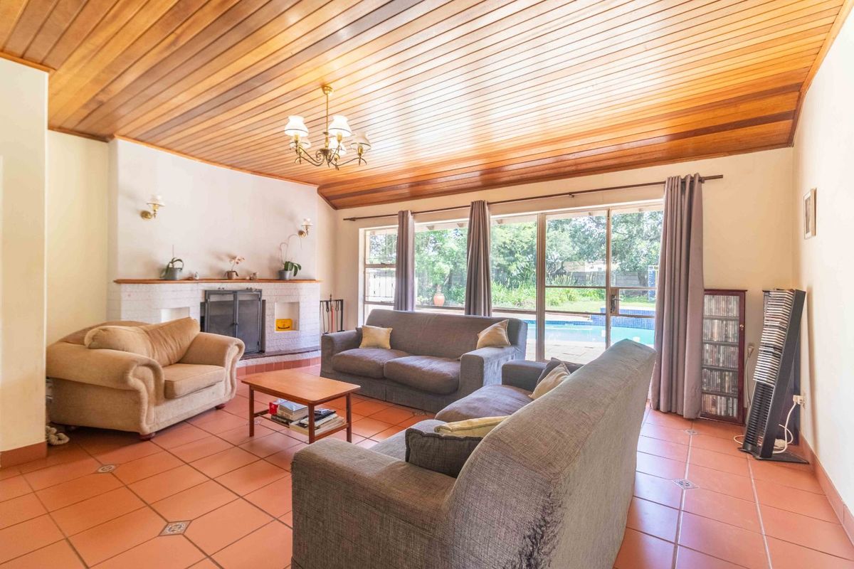 Spacious living room featuring a brick fireplace, terracotta tiled flooring, and a timber-paneled ceiling with direct access to the outdoor pool area.